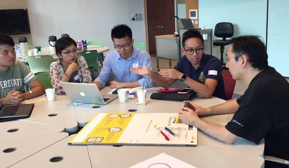 Participants and a mentor talking around a table during a B4B Challenge team session